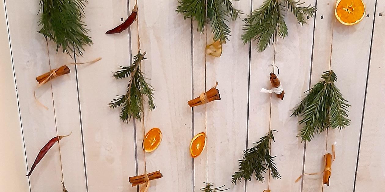 small green fir branches, dried orange slices and cinnamon stick tied to string hanging from a short sick and displayed indoors