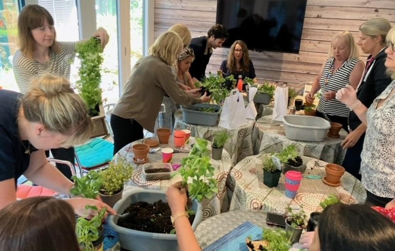 woman holding up herb pot in group around table