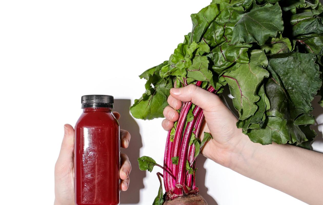 purple beetroot vegetable with green leaves and stalks and bottle of purple beetroot juice 